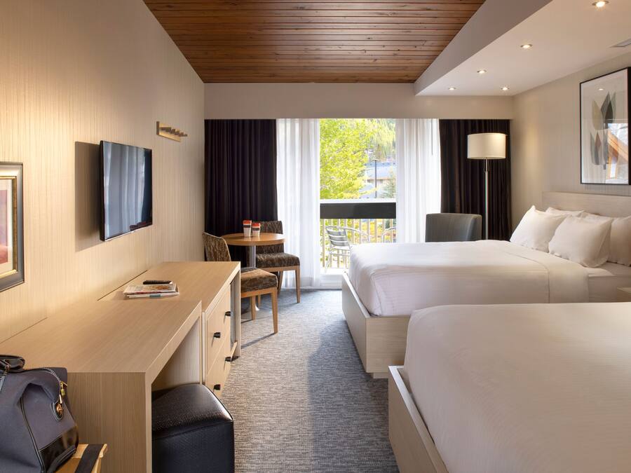 Une chambre d’hôtel avec deux lits, un bureau, une chaise, une lampe et une fenêtre avec des rideaux.