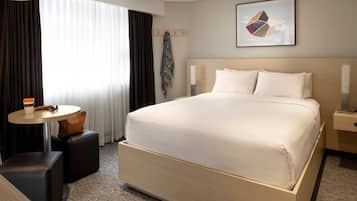 Quarto de hotel com uma cama grande, uma mesa redonda com uma xícara de café e um cabideiro.