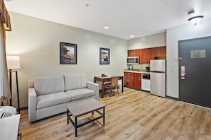 Una habitación de hotel moderna con un sofá, una mesita, una kitchenette y una puerta.