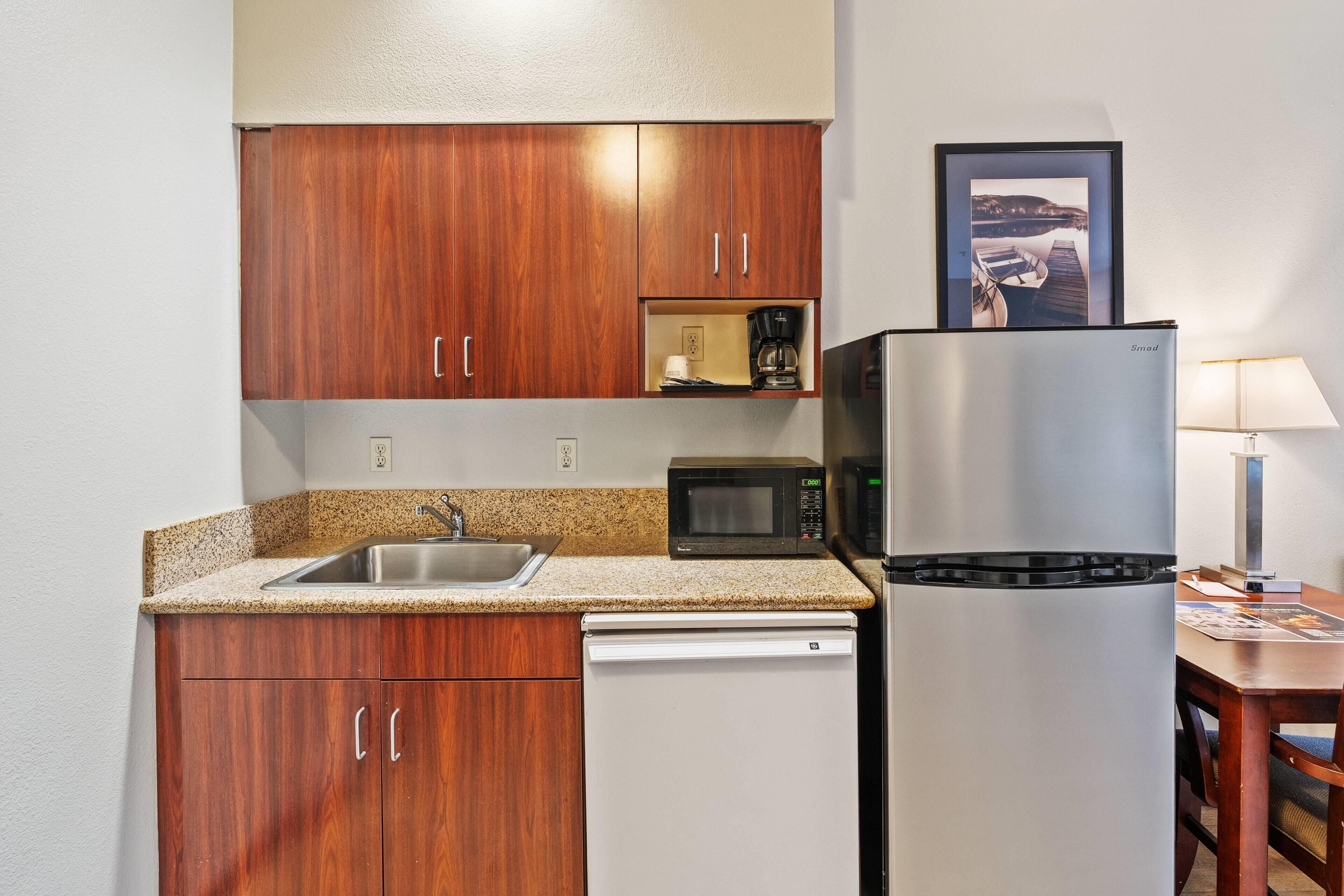 A compact kitchen with wooden cabinets, a stainless steel refrigerator, a microwave, and a coffee maker.