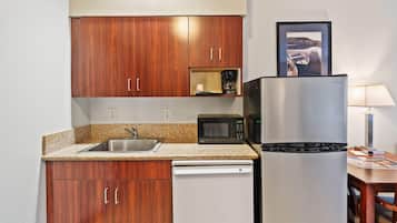 A compact kitchen with wooden cabinets, a stainless steel refrigerator, a microwave, and a coffee maker.
