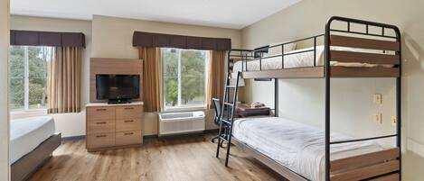 A hotel room with a bunk bed, a desk with a computer, a TV, and a window with curtains.