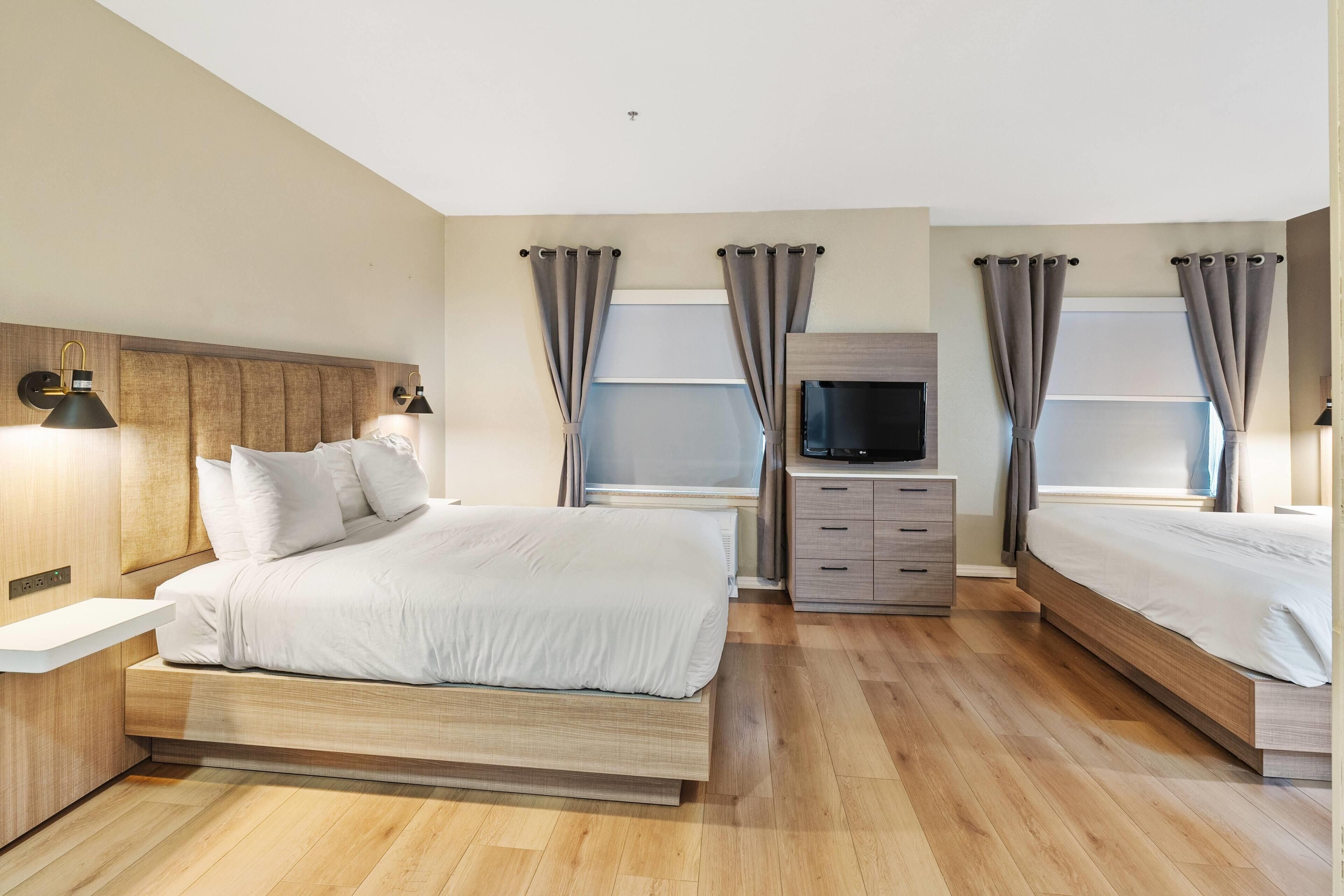 Een moderne hotelkamer met een groot bed, nachtkastjes, een televisie en gordijnen.