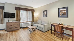 Una habitación amoblada con sofá, escritorio, televisor, cómoda y ventana con cortinas.