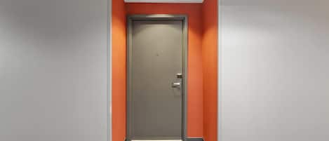 A hallway with a door, carpeted floor, and walls painted in grey and orange.