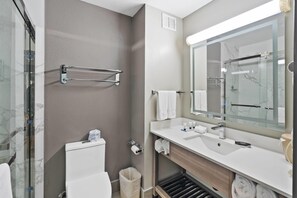 Een moderne badkamer met een glazen douche, een witte wastafel, een grote spiegel en een handdoekrek.