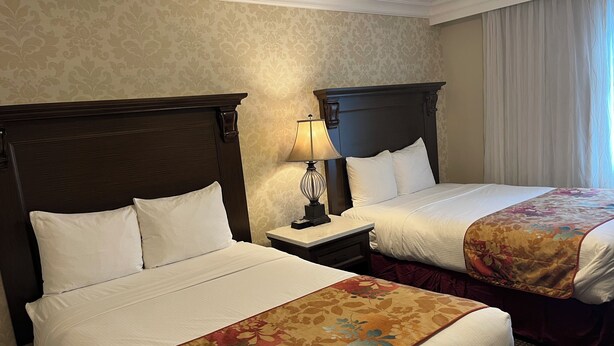 Una habitación de hotel con dos camas, una mesita de noche con lámpara y una ventana con cortinas.