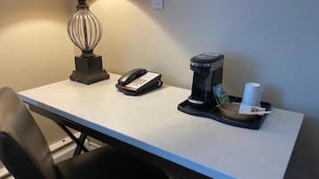 Escritorio de habitación de hotel con lámpara, teléfono, cafetera y bandeja con taza y pañuelos.