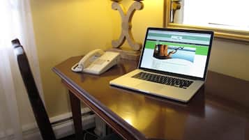 A laptop on a wooden desk with a telephone and a decorative lamp.