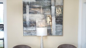 Una habitación moderna con dos sillones, un cuadro abstracto grande, una araña y una mesa con una lámpara.