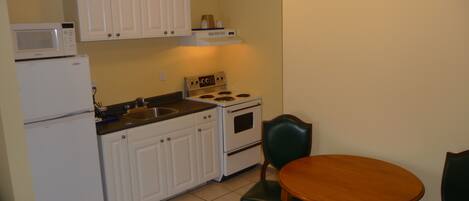 A compact kitchen with white cabinets, a microwave, a stove, and a dining table with chairs.