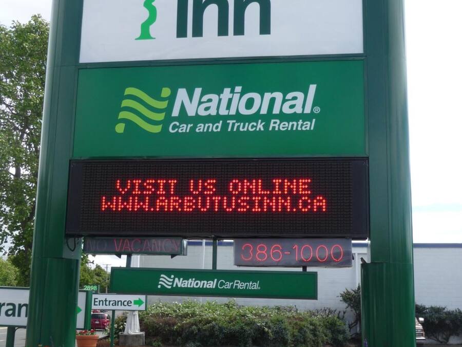 A sign for Arbutus Inn with a National Car Rental logo and a digital display advertising online booking.