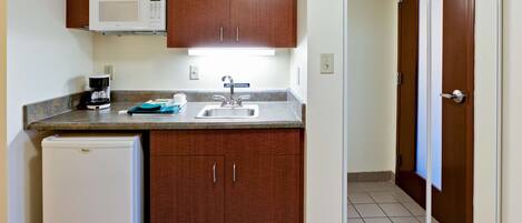 A compact kitchen with a microwave, coffee maker, sink, and a refrigerator.