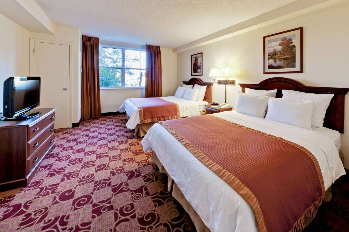 A hotel room with two beds, a TV, a desk, and a window with curtains.