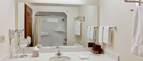Un baño de hotel con un espejo grande, un lavamanos, una ducha y varias toallas.
