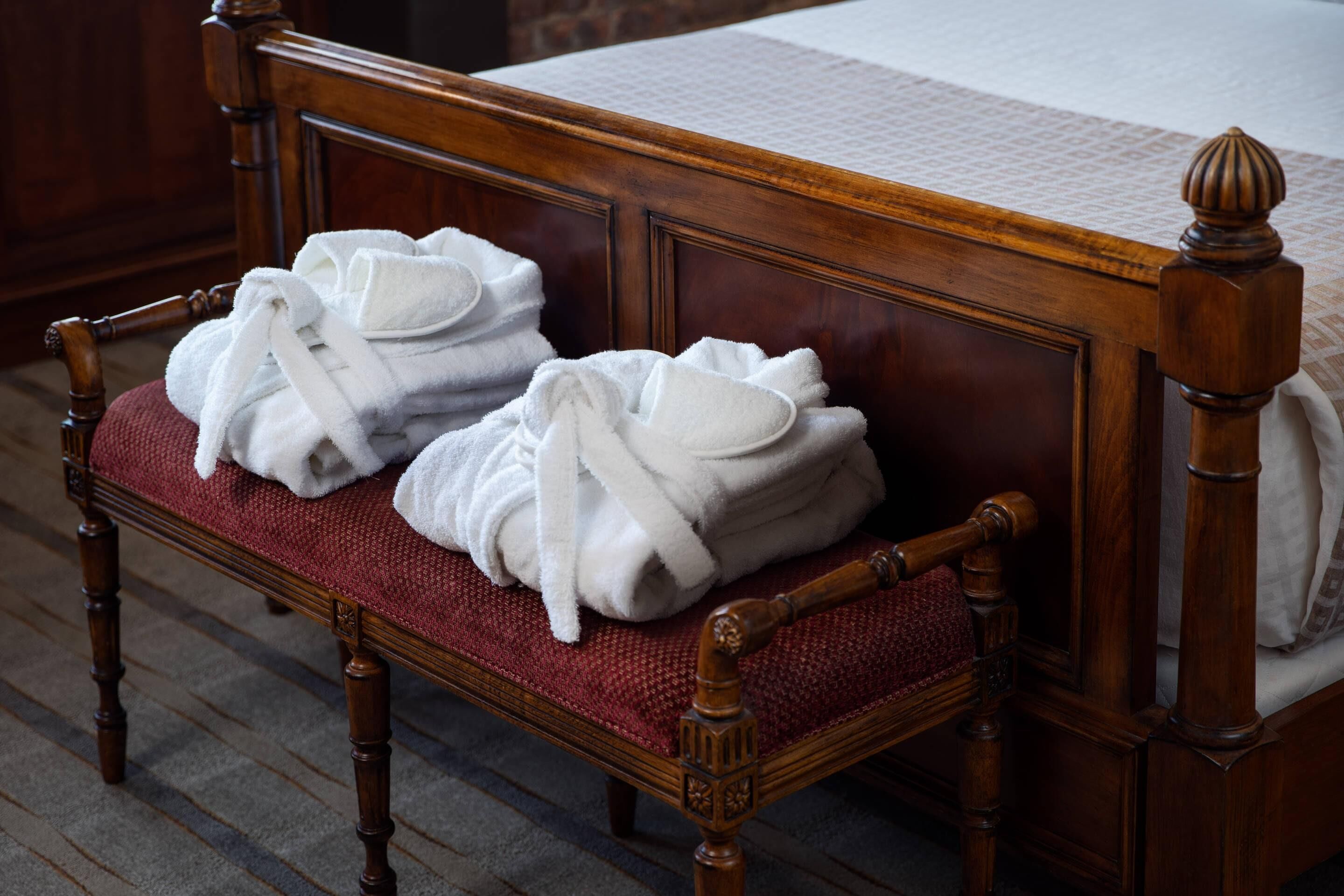 Una cama de madera con cabecera y piecera tapizados en rojo, y dos toallas blancas sobre la cabecera.