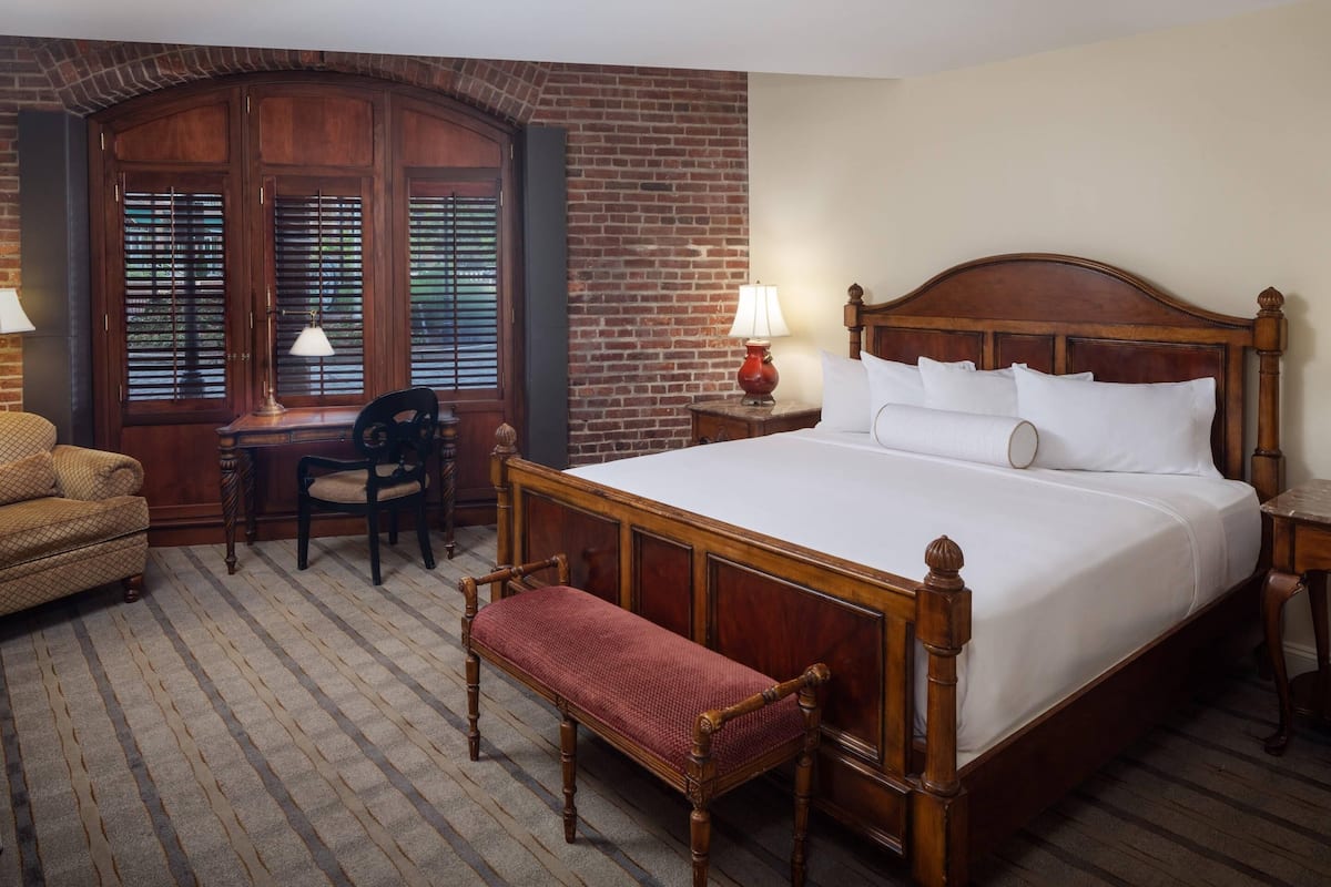 A hotel room with a large wooden bed, a bench, a desk, and a chair.