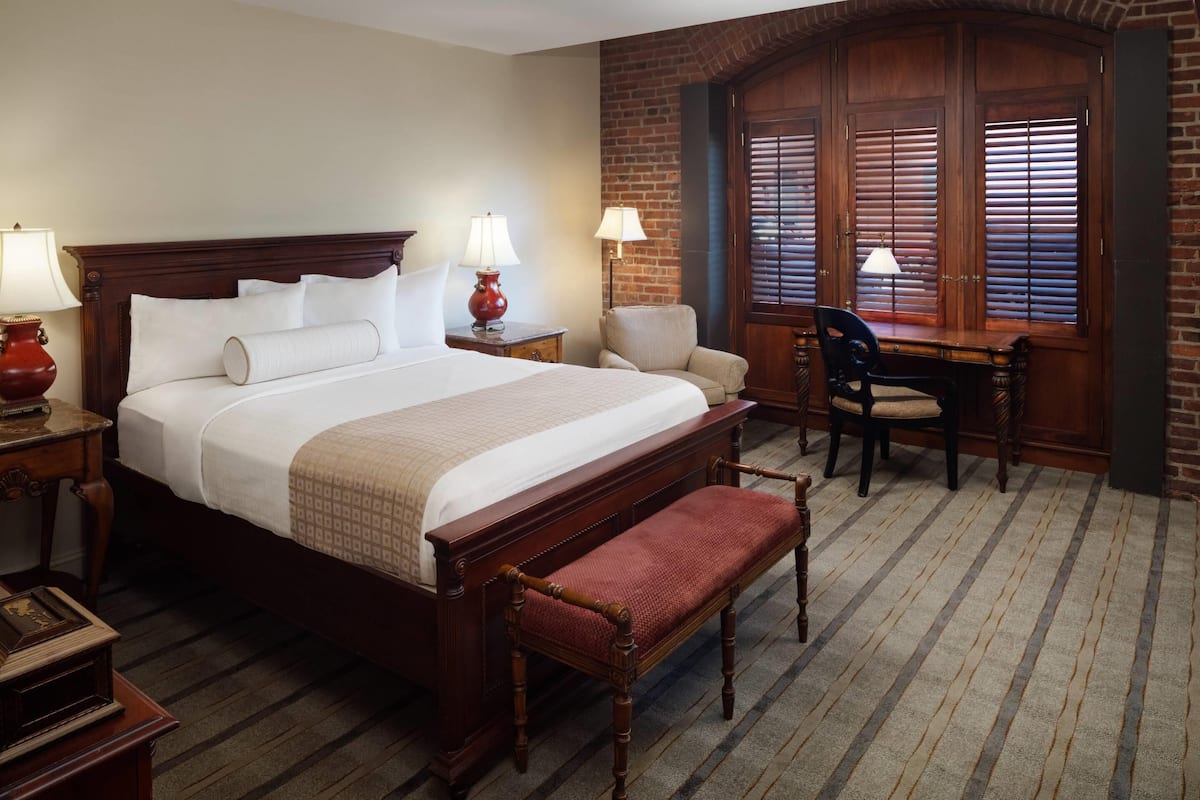 A hotel room with a large bed, a desk, a chair, and a bench.