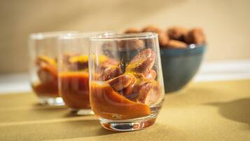 Tres vasos con bebida y rodajas de naranja, sobre una mesa con un tazón de nueces al fondo.