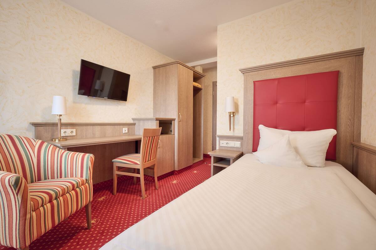 A hotel room with a bed, a desk, a chair, a television, and a wardrobe.