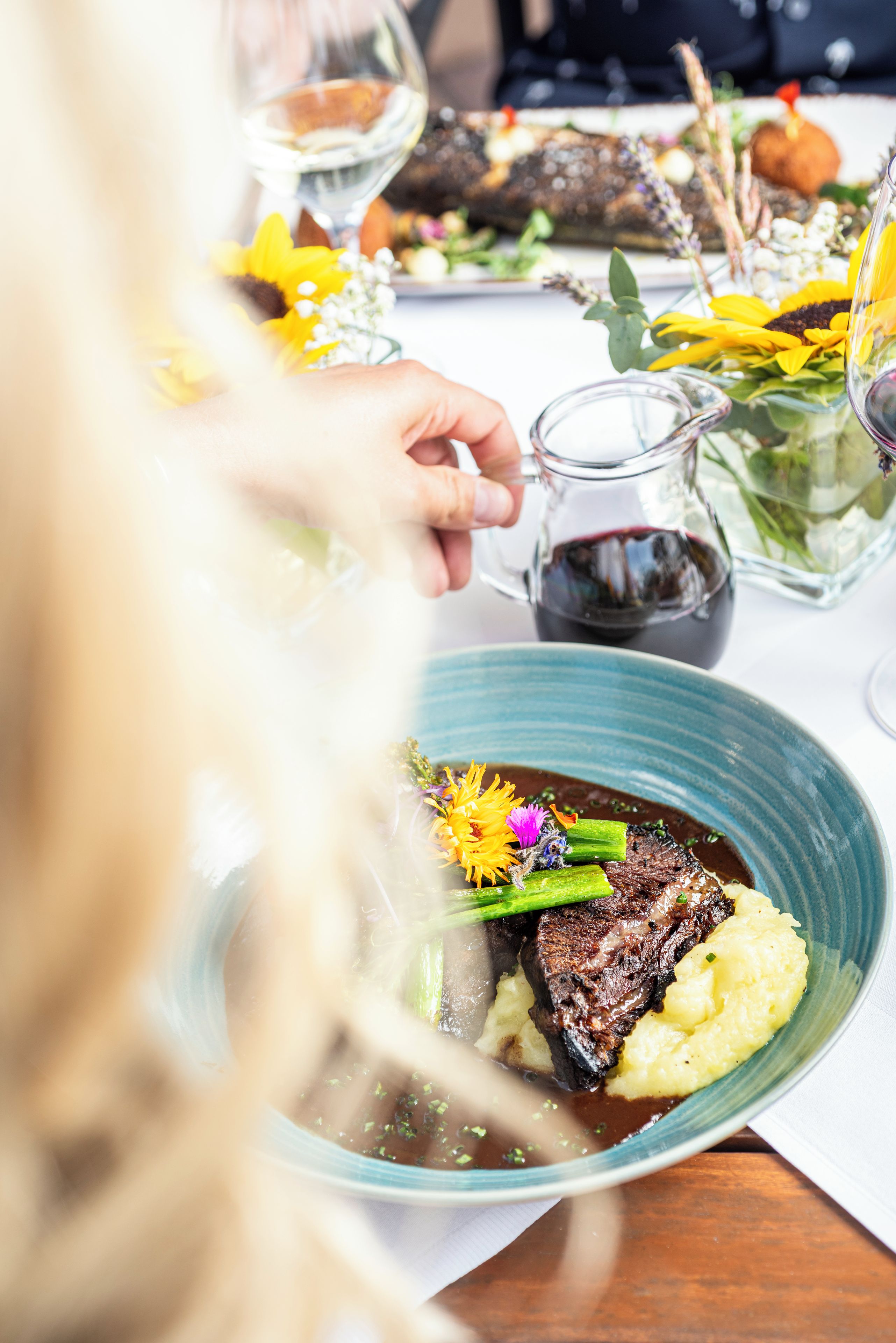 Une table à manger avec une assiette de nourriture, une carafe et un vase rempli de fleurs.