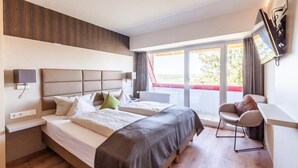 Habitación de hotel con dos camas, un escritorio, una silla y un ventanal con vistas.