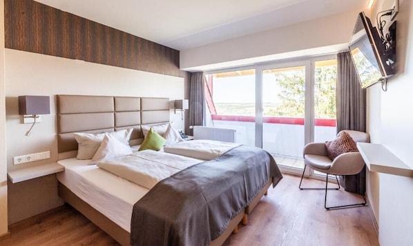 Habitación de hotel con dos camas, un escritorio, una silla y un ventanal con vistas.