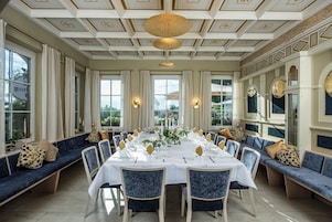 A formal dining room with a long table set for a meal, surrounded by blue upholstered seating.