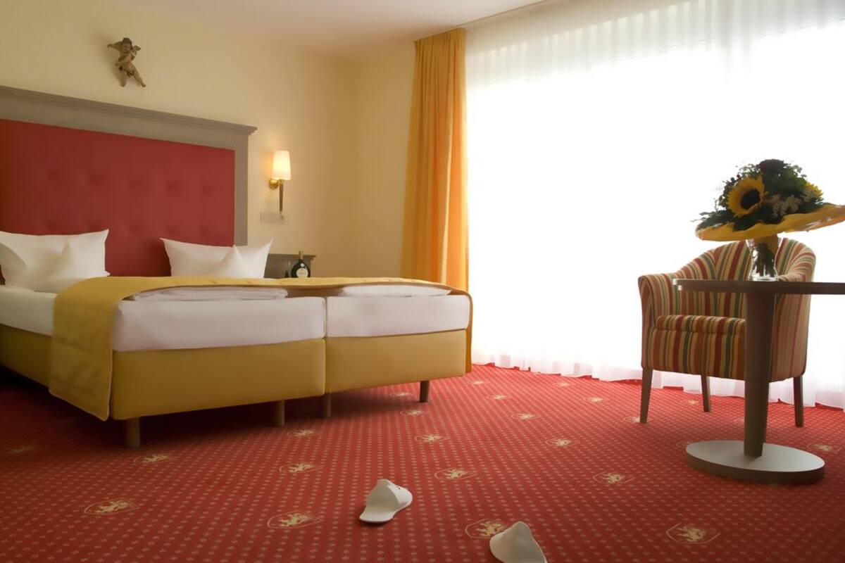 A hotel room with a double bed, a small table with a vase of flowers, and a chair.