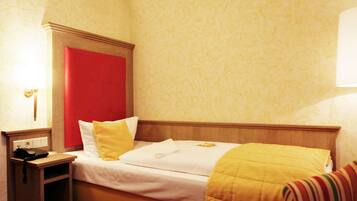 A hotel room with a bed, a nightstand, a lamp, and a red accent wall.