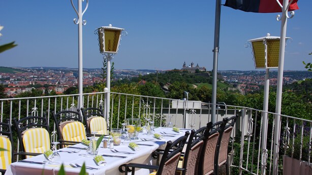 Una mesa lista para comer, con sillas, una bandera y una vista panorámica de la ciudad de fondo.