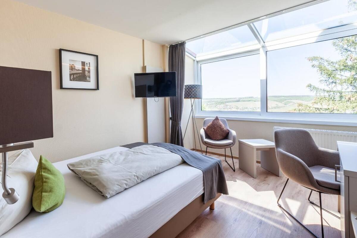 A hotel room with a bed, a desk, a chair, a TV, and a window with a view.