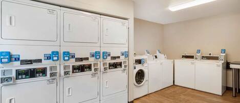 A laundry facility with multiple washing machines and dryers, each with control panels and labels.