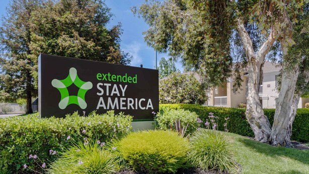 Extended Stay America -hotelliketjun kyltti, jossa on sen logo. Kyltin ympärillä on hoidettua viheraluetta ja puita.