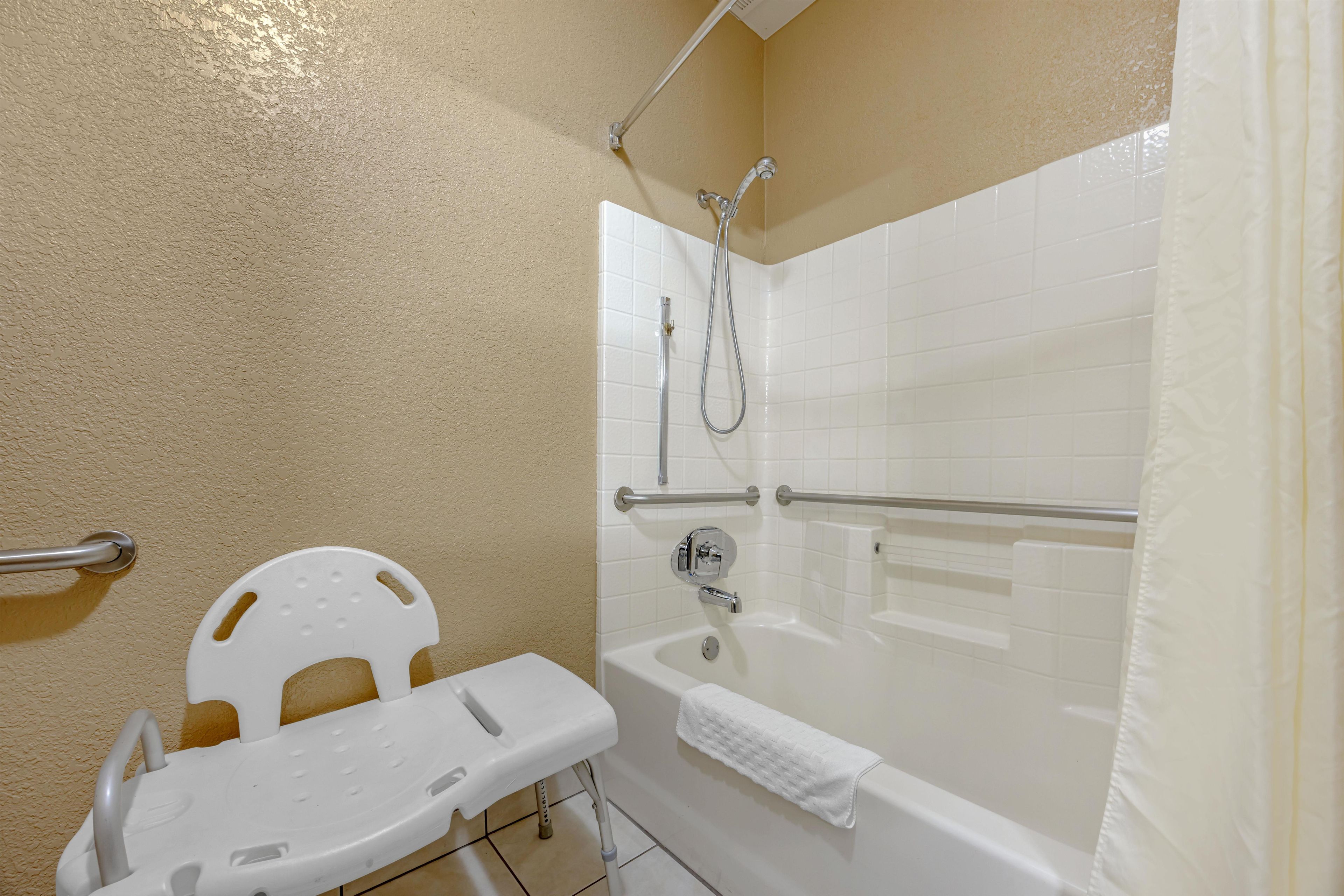 Un baño con una bañera blanca, ducha con cabezal de ducha de mano y barra de apoyo blanca.