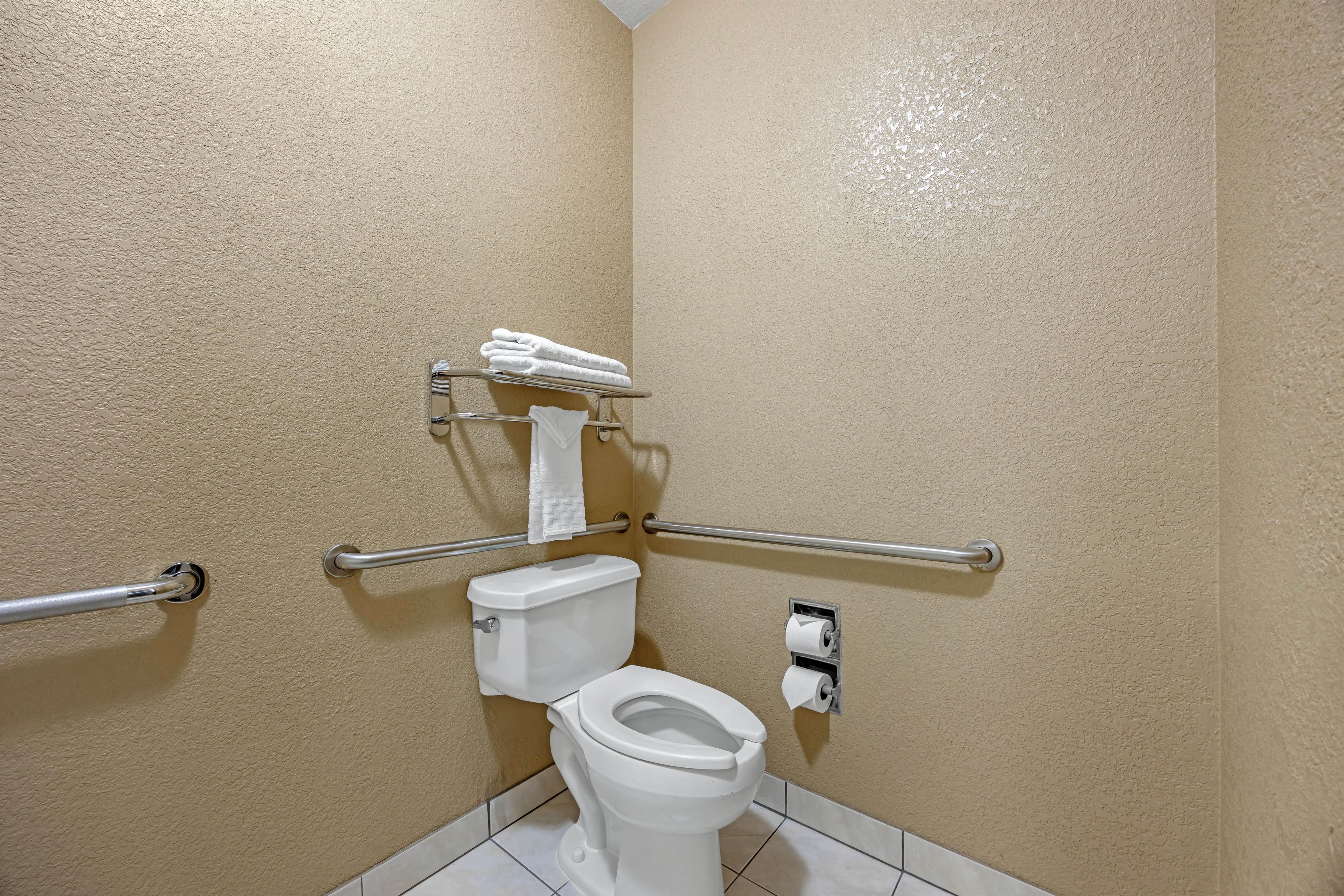A small, single-occupancy bathroom with a toilet, handrails, and a towel rack.