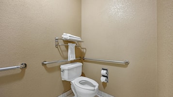 A small, single-occupancy bathroom with a toilet, handrails, and a towel rack.