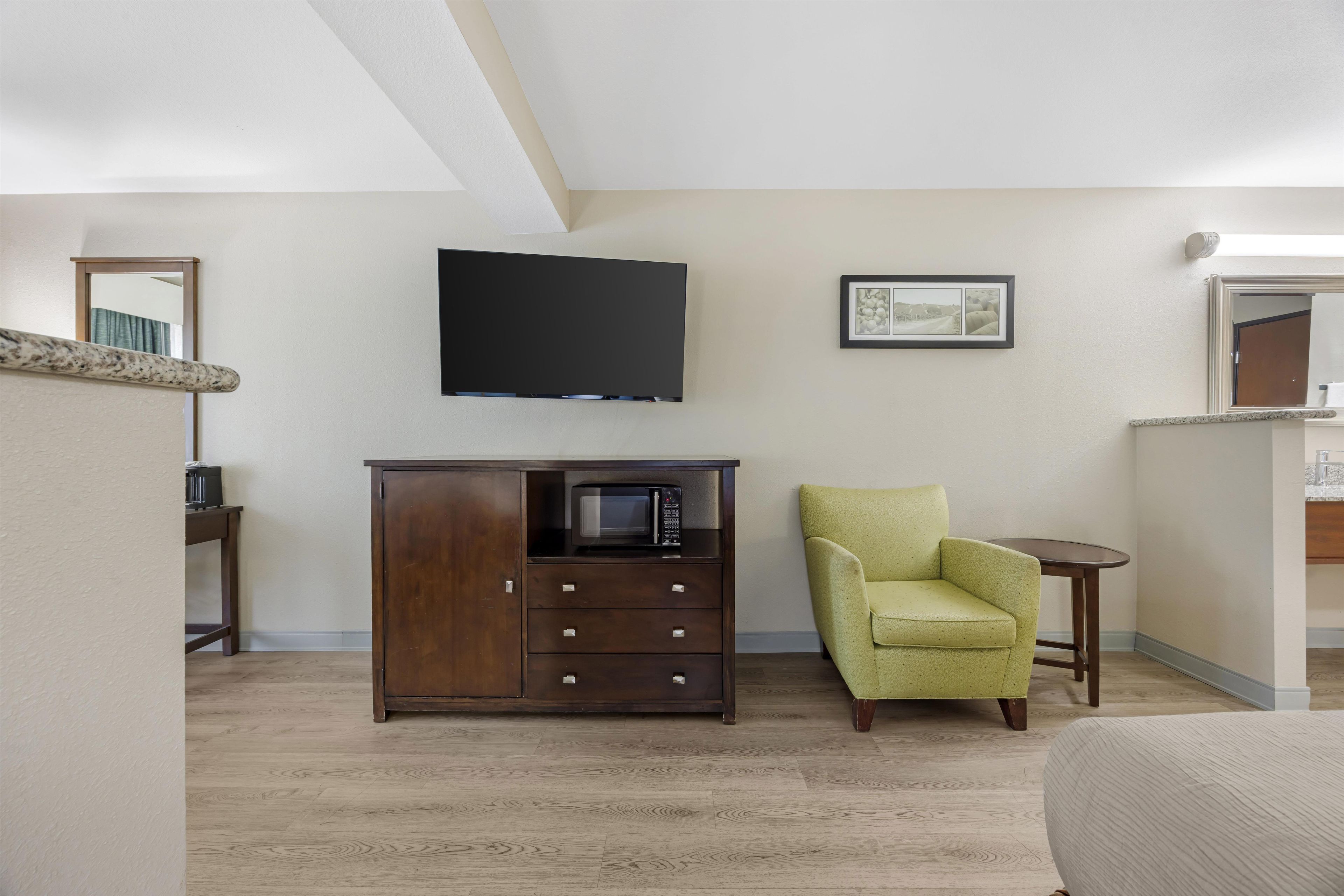 A room with a wooden cabinet, a green armchair, a small table, and a flat-screen TV mounted on the wall.