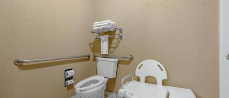 Casa de banho com sanita, balaustre, barra de apoio, suporte de papel higiénico branco e cadeira de plástico branca.