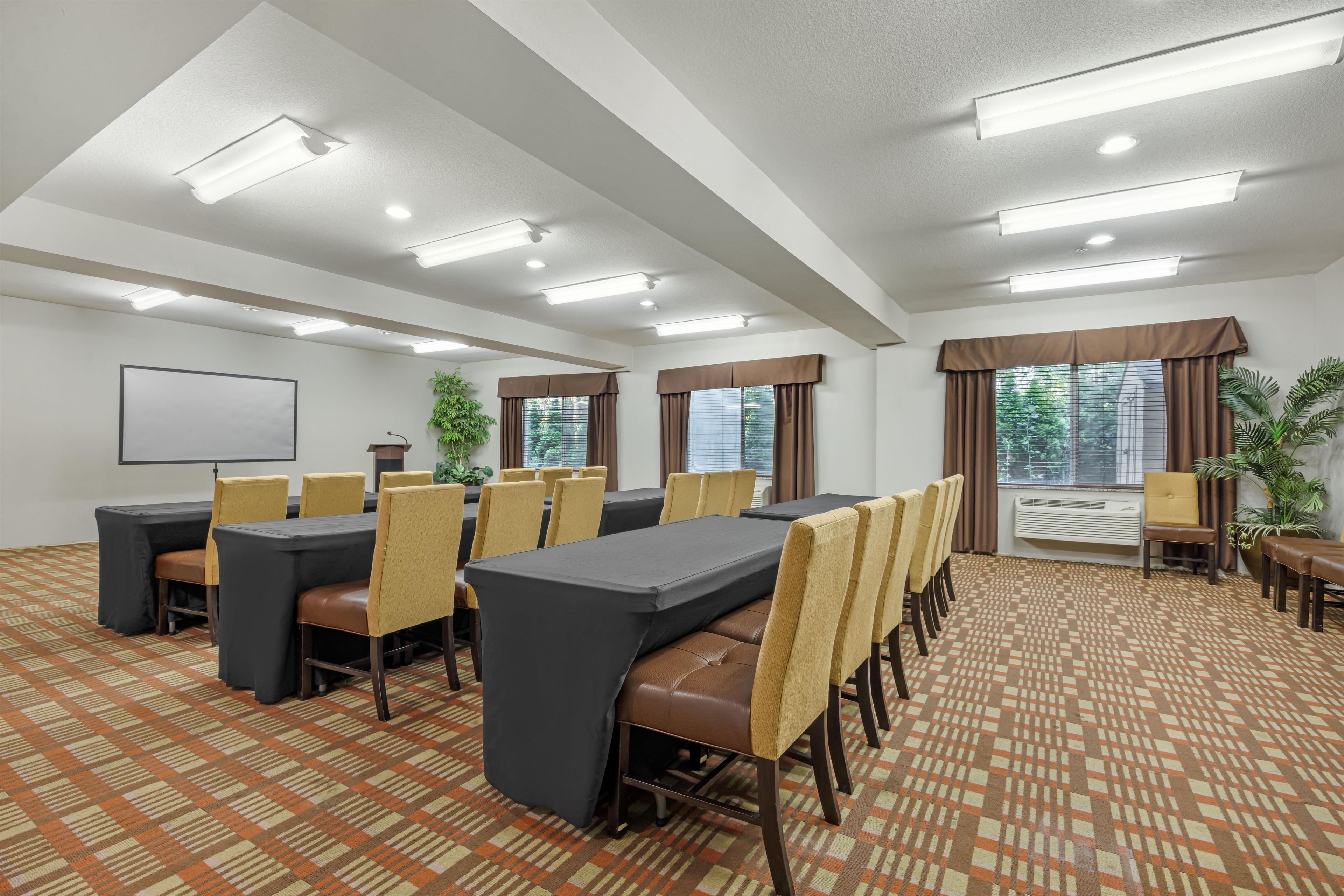 A conference room with tables and chairs, a projector screen, and windows with curtains.