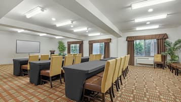 A conference room with tables and chairs, a projector screen, and windows with curtains.