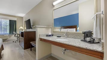 A hotel bathroom with a granite countertop, a sink, a mirror, a towel rack, and a coffee machine.