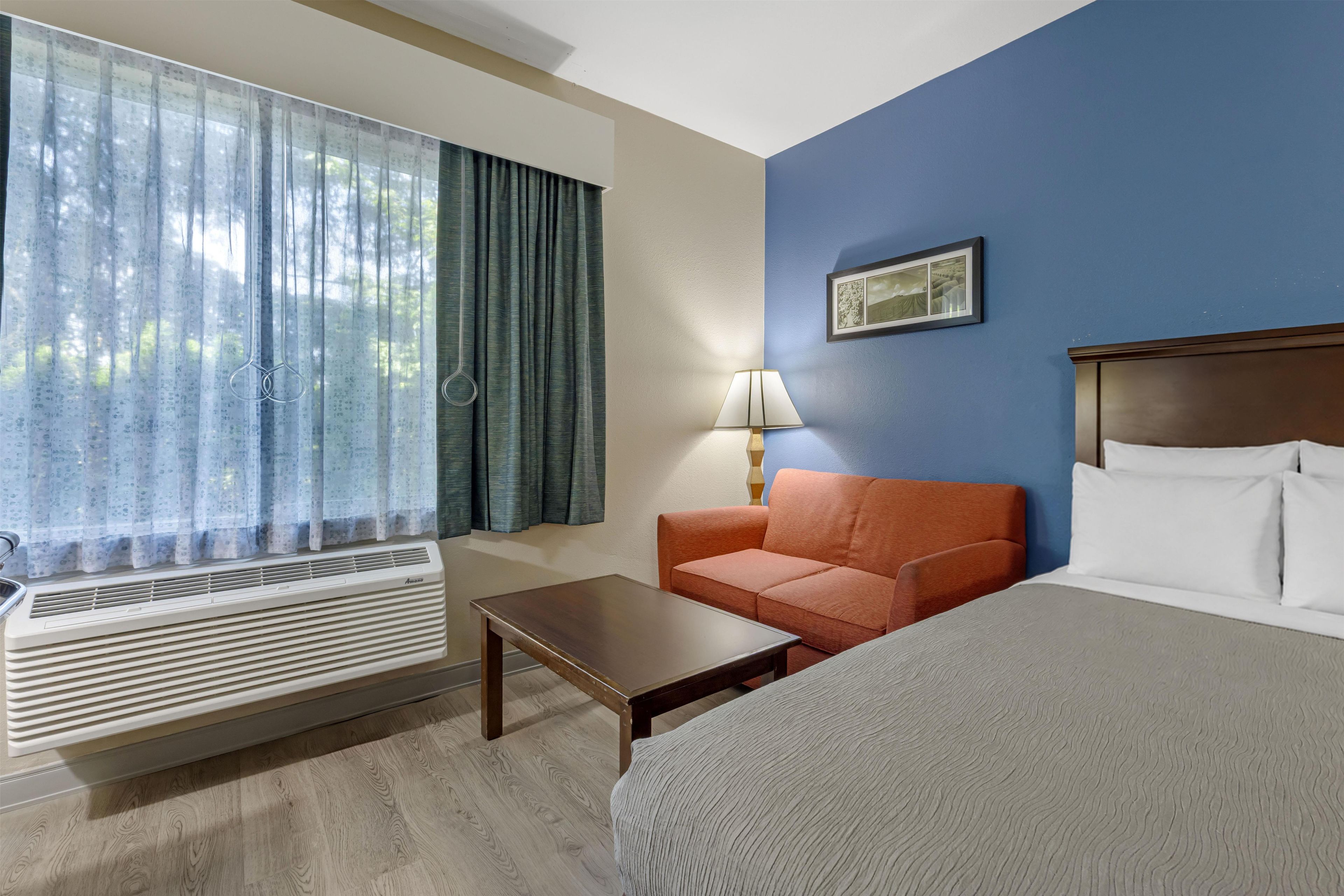 Une chambre d’hôtel avec un lit, un canapé, une table, une lampe et une fenêtre avec des rideaux.