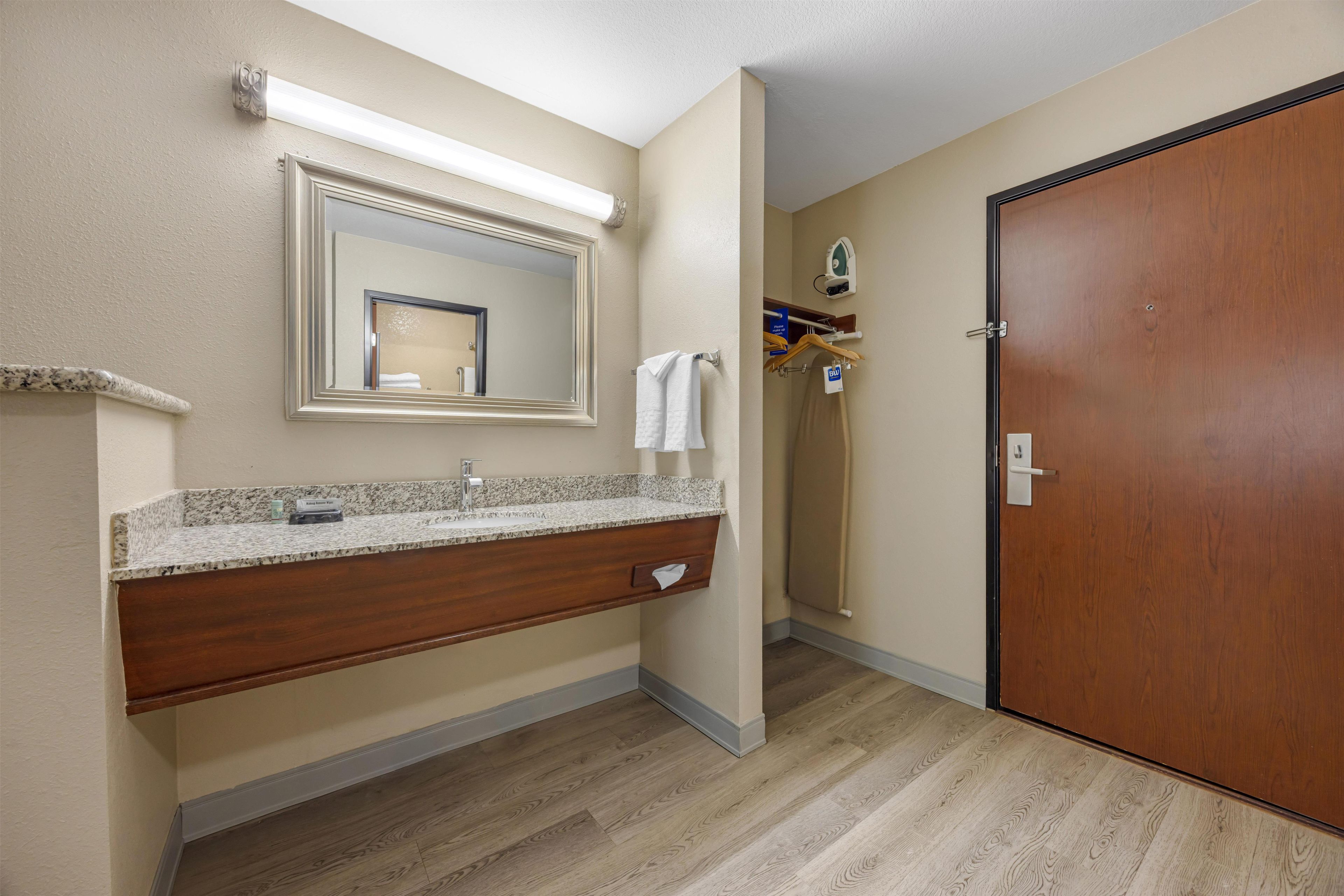 A hotel bathroom with a granite countertop sink, a mirror, a towel rack, and a wooden door.