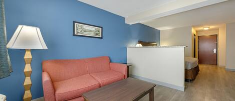 Une pièce avec un canapé rouge, une table basse en bois, une lampe et un tableau encadré au mur.