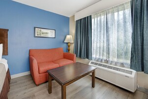 Habitación de hotel con pared azul, sofá rojo, mesa de madera, lámpara y ventana con cortinas.