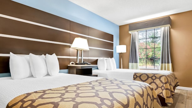 A hotel room with two beds, a nightstand, a lamp, and a window with curtains. - Baymont by Wyndham Forest City (Forest City)