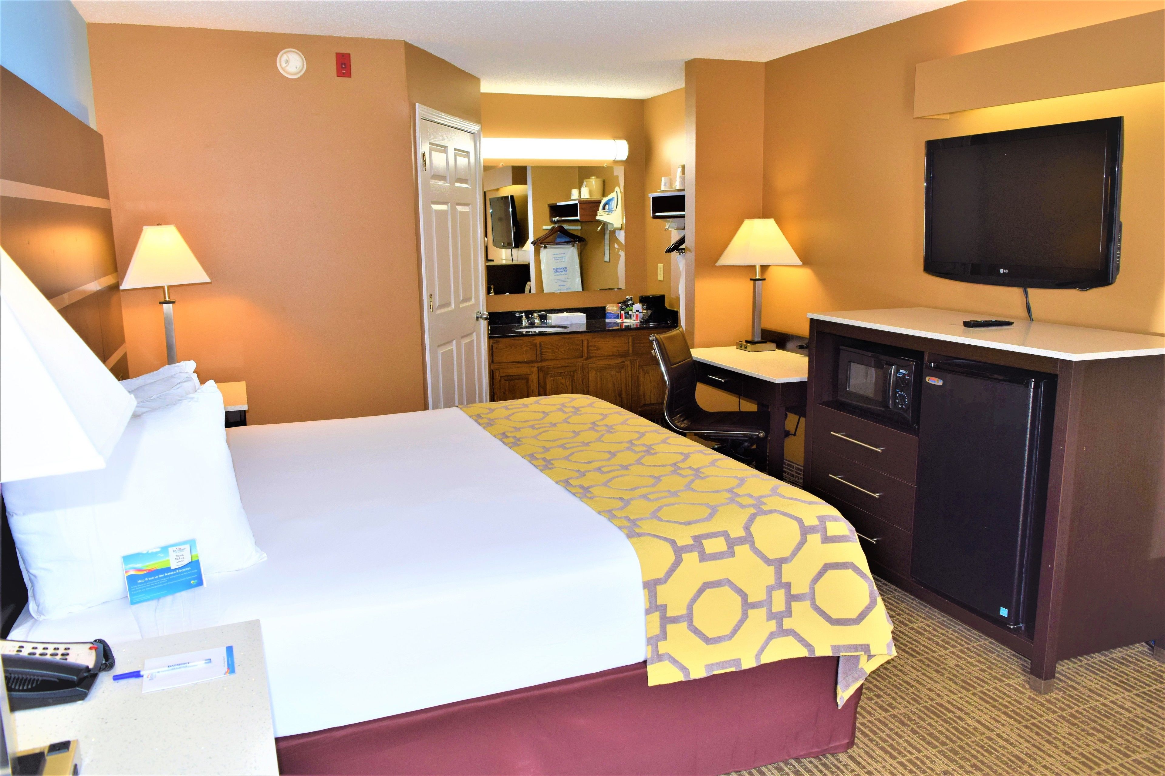 A hotel room with a bed, desk, microwave, and TV.