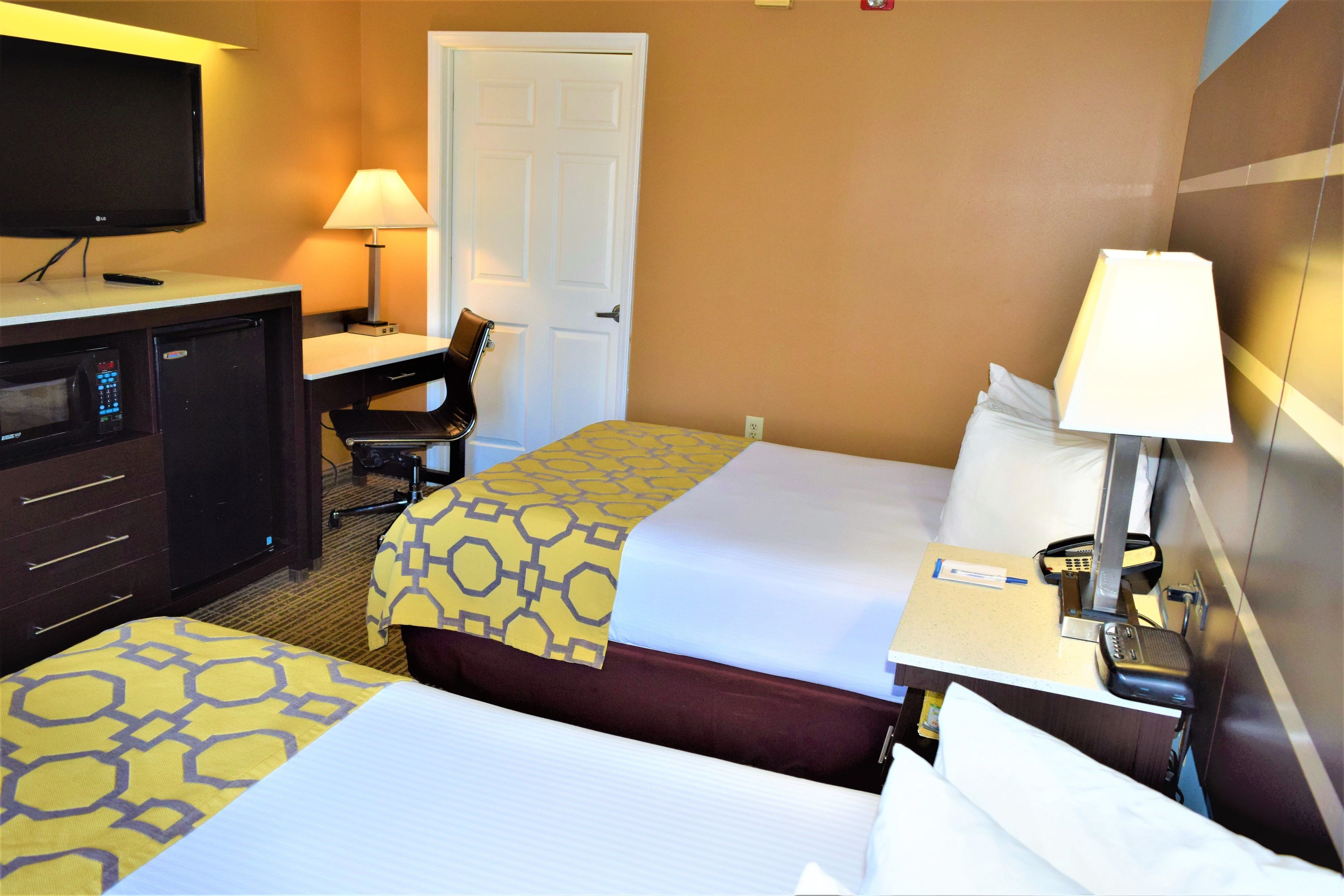 A hotel room with two beds, a desk, a television, and a lamp.