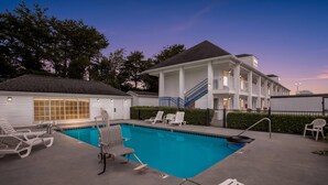 A swimming pool with lounge chairs, a covered deck, and a building with a staircase and balcony. - Baymont by Wyndham Forest City (Forest City)